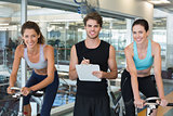 Fit women in a spin class with trainer smiling at camera