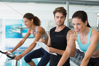 Fit women in a spin class with trainer taking notes