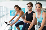 Fit women in a spin class with trainer taking notes and smiling at camera