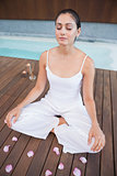 Peaceful brunette in white sitting in lotus pose surrounded by petals