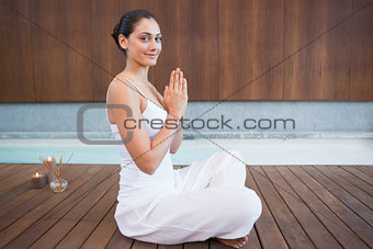Content brunette in white sitting in lotus pose smiling at camera