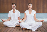 Attractive couple in white sitting in lotus pose smiling at camera
