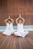 Attractive couple in white sitting in lotus pose with hands together