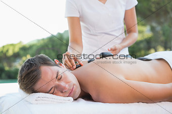 Handsome man getting a hot stone massage poolside