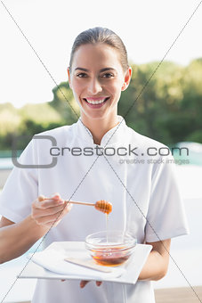 Smiling beauty therapist looking at camera holding plate with honey