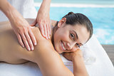 Smiling brunette getting a massage poolside looking at camera