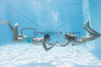 Cute couple holding hands underwater in the swimming pool
