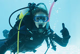 Woman on scuba training submerged in swimming pool showing thumbs up