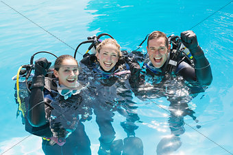 Smiling friends on scuba training in swimming pool cheering at camera