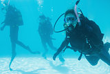 Friends on scuba training submerged in swimming pool one looking to camera