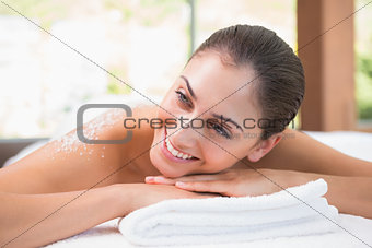 Beautiful smiling brunette lying on massage table with salt scrub on back