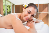 Beautiful smiling brunette lying on massage table with salt scrub on back