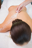 Beauty therapist pouring salt scrub on womans back