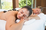 Calm friends lying on massage tables with hot stones on their backs