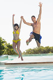 Excited couple jumping into swimming pool on holidays