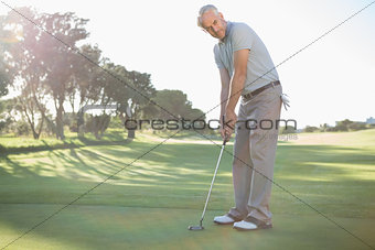 Handsome golfer putting ball on the green