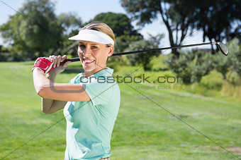 Female golfer taking a shot and smiling at camera