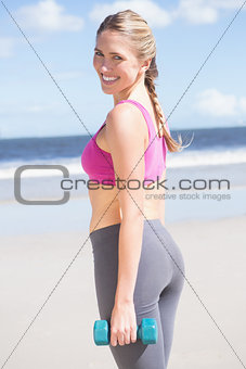 Fit woman working out with dumbbells on the beach smiling at camera
