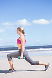 Fit woman working out with dumbbells on the beach lunging