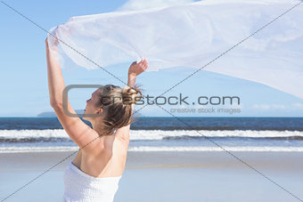 Pretty blonde holding up white shawl on the beach