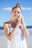 Pretty blonde in white dress listening to conch on the beach