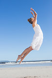 Pretty blonde in white dress leaping on the beach