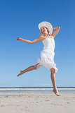 Pretty blonde in white dress leaping on the beach