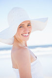 Pretty smiling blonde in white dress and sunhat on the beach
