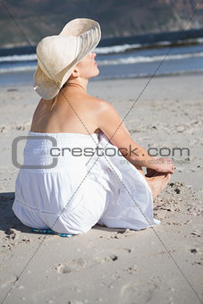 Content blonde in white dress sitting on the beach