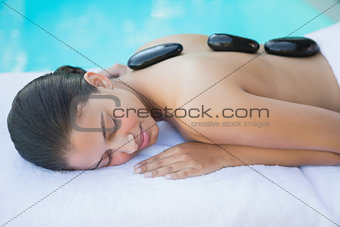 Relaxed brunette lying poolside having a hot stone massage
