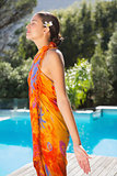 Brunette in sarong standing with arms out by the pool