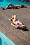 Women in bikinis lying poolside sunbathing