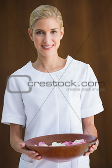 Smiling beauty therapist holding bowl of rose petals
