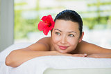 Smiling brunette lying on massage table with red lily in her hair