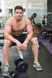 Handsome bodybuilder sitting on bench in weights room
