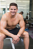 Handsome smiling bodybuilder sitting on bench in weights room