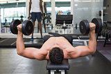 Shirtless bodybuilder lying on bench lifting heavy dumbbells