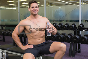Shirtless bodybuilder sitting on bench with water bottle