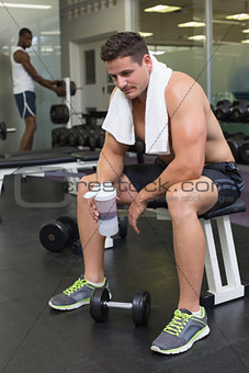 Shirtless bodybuilder holding protein drink sitting on bench