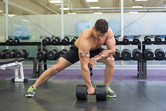 Shirtless bodybuilder lifting heavy black dumbbell in a lunge