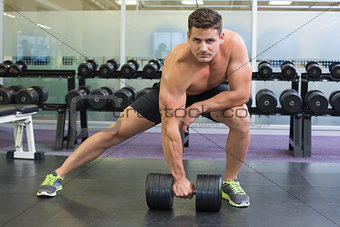 Shirtless bodybuilder lifting heavy black dumbbell in a lunge