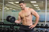 Shirtless bodybuilder lifting heavy black dumbbell looking at camera