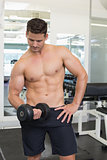 Shirtless focused bodybuilder lifting heavy black dumbbell