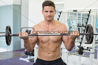Shirtless bodybuilder lifting heavy barbell weight looking at camera