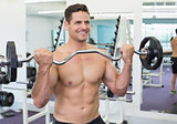 Shirtless smiling bodybuilder lifting heavy barbell weight