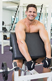 Shirtless smiling bodybuilder lifting heavy barbell weight using bench