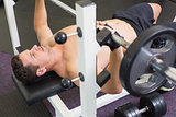 Shirtless bodybuilder lifting heavy barbell weight lying on bench