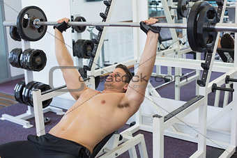 Shirtless bodybuilder lifting heavy barbell weight lying on bench