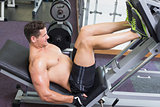 Shirtless bodybuilder working on his legs with weight machine