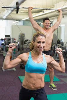 Happy muscular man and woman lifting weights